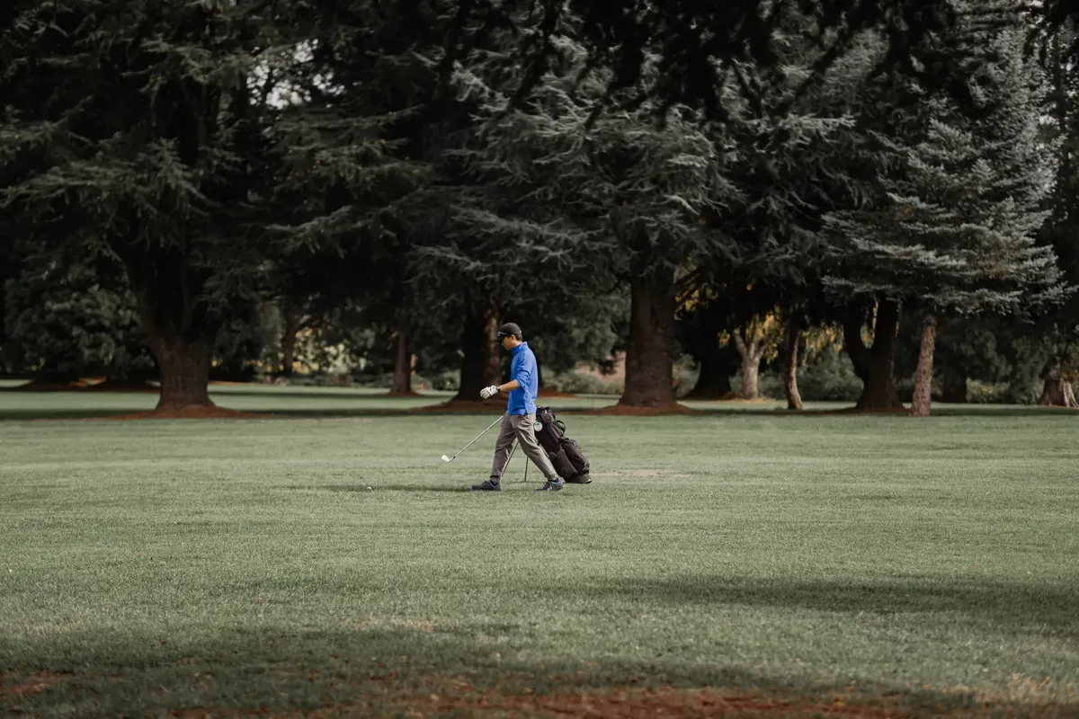 A golfer enjoying a sunny day on a lush green golf course surrounded by trees.