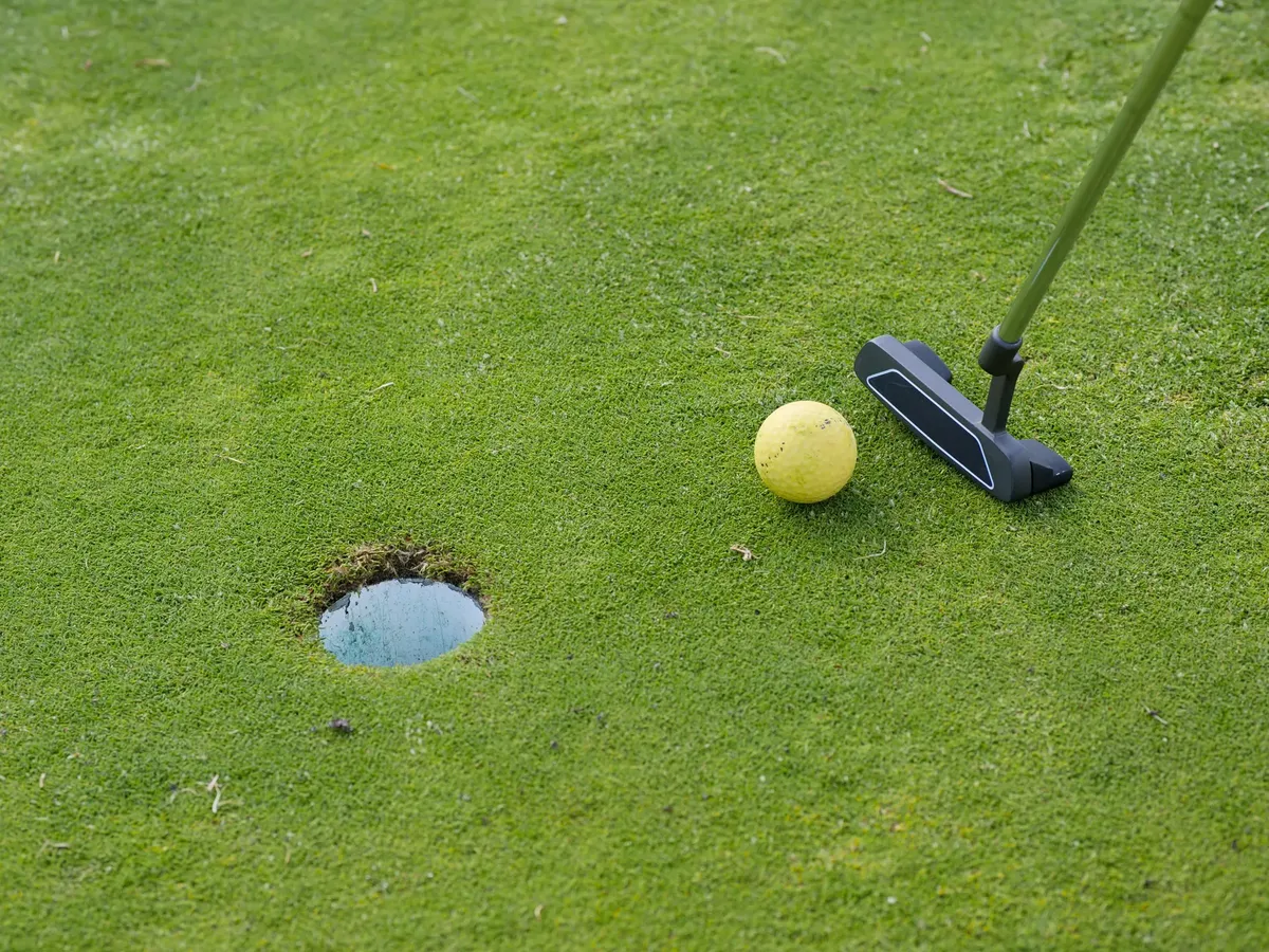 A golf ball and putter near a hole on a lush green golf course, ready for a putt.